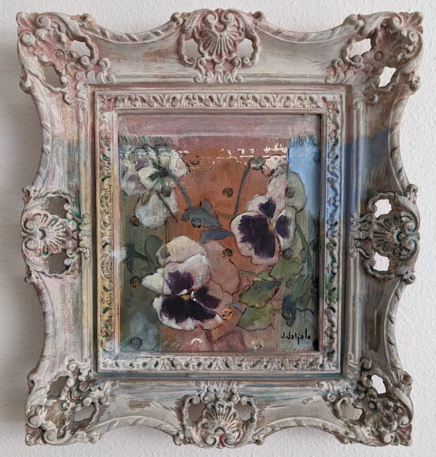White and purple pansies on a terracotta ground within an ornate pale carved frame.