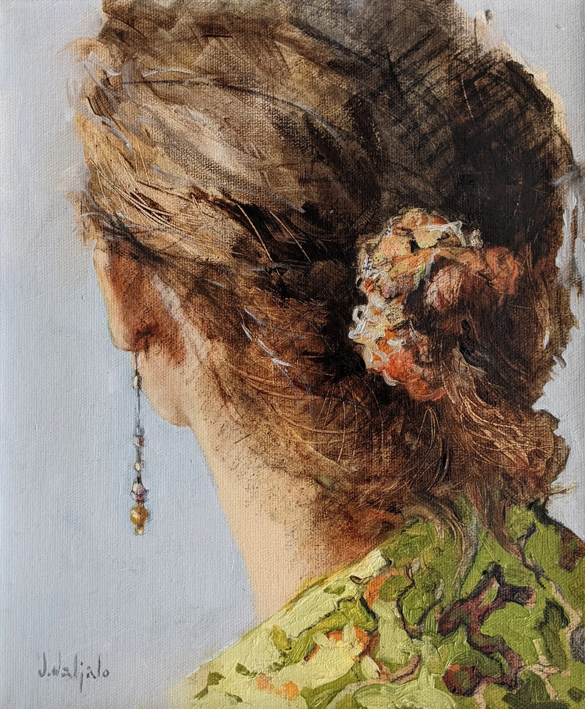 A woman seen from behind with a flower in her brown bun and green patterning at her shoulder.