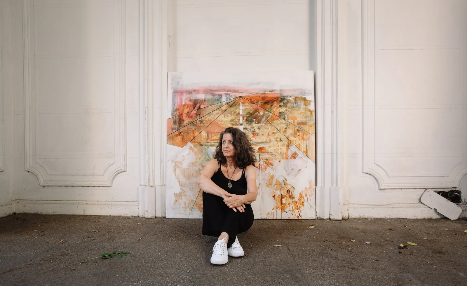 Victoria Valjalo seated in front of a large abstract painting against a white panelled wall.